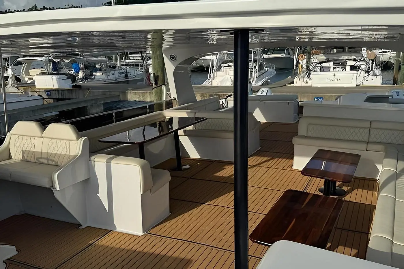 Covered main deck of a power catamaran with helm seats, cream sofas and small wooden tables