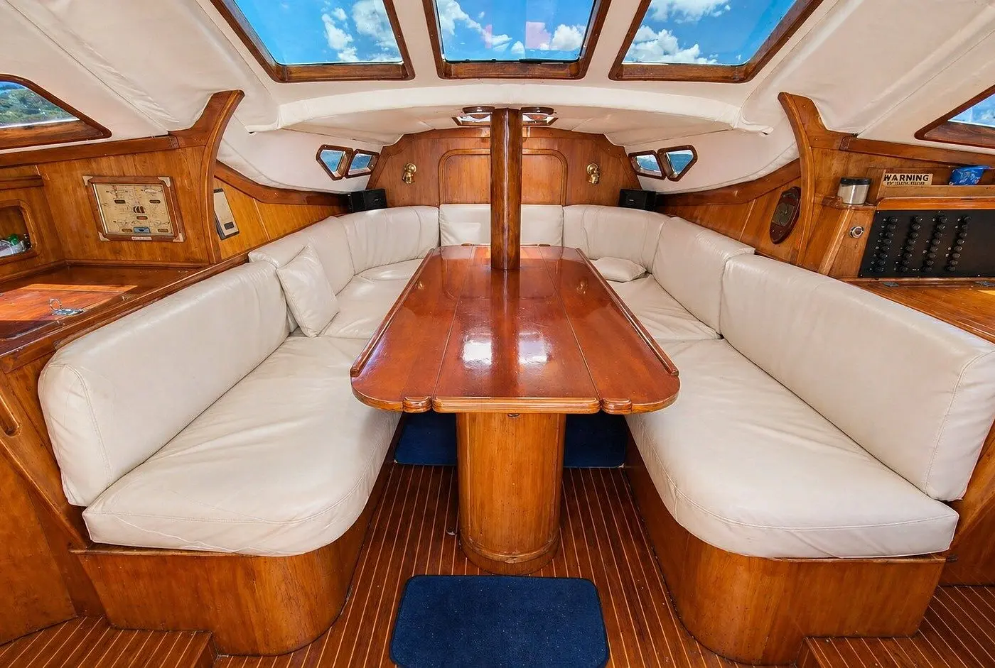 Below-deck saloon with white U-shaped seating around a varnished wood table, skylights overhead