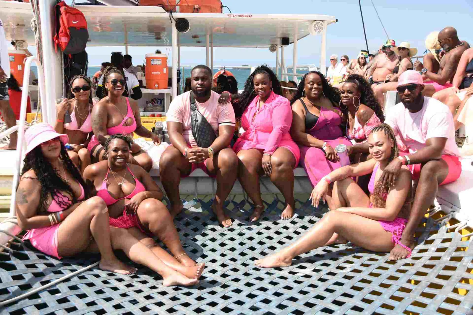 Friends dressed in pink sitting on the deck and net of a catamaran under its shade canopy