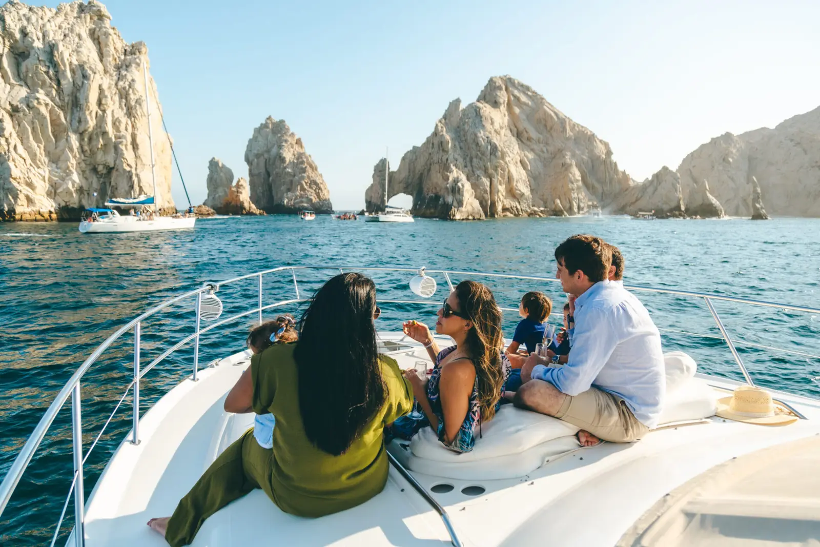 A family relaxes on the yacht's bow as it approaches the rock formations of Cabo San Lucas