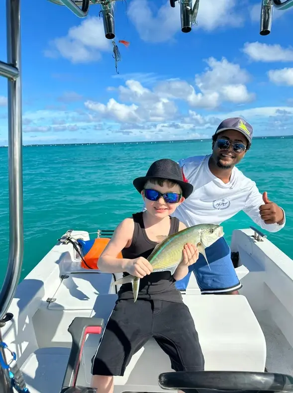 Child in a bucket hat holding a fish as a crew member gives a thumbs-up