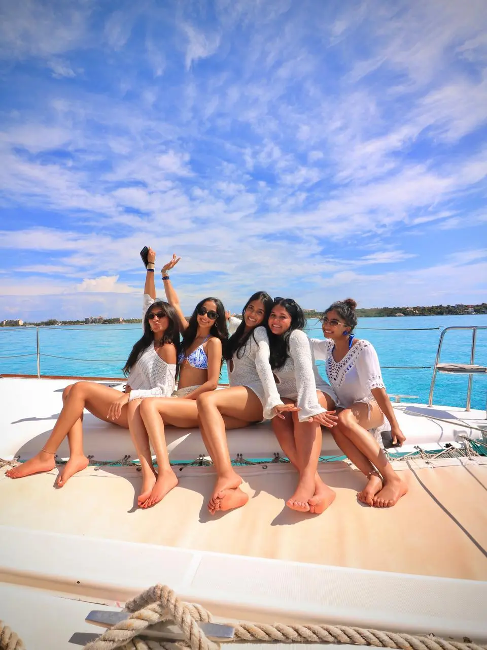 Group of women in white cover-ups posing on the bow of a catamaran with open sea behind