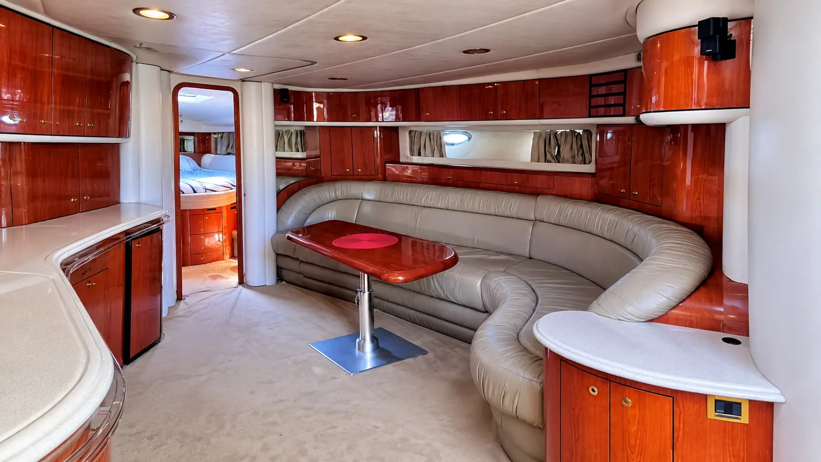Saloon with a curved cream leather sofa, red table and cherry wood cabinetry on a motor yacht