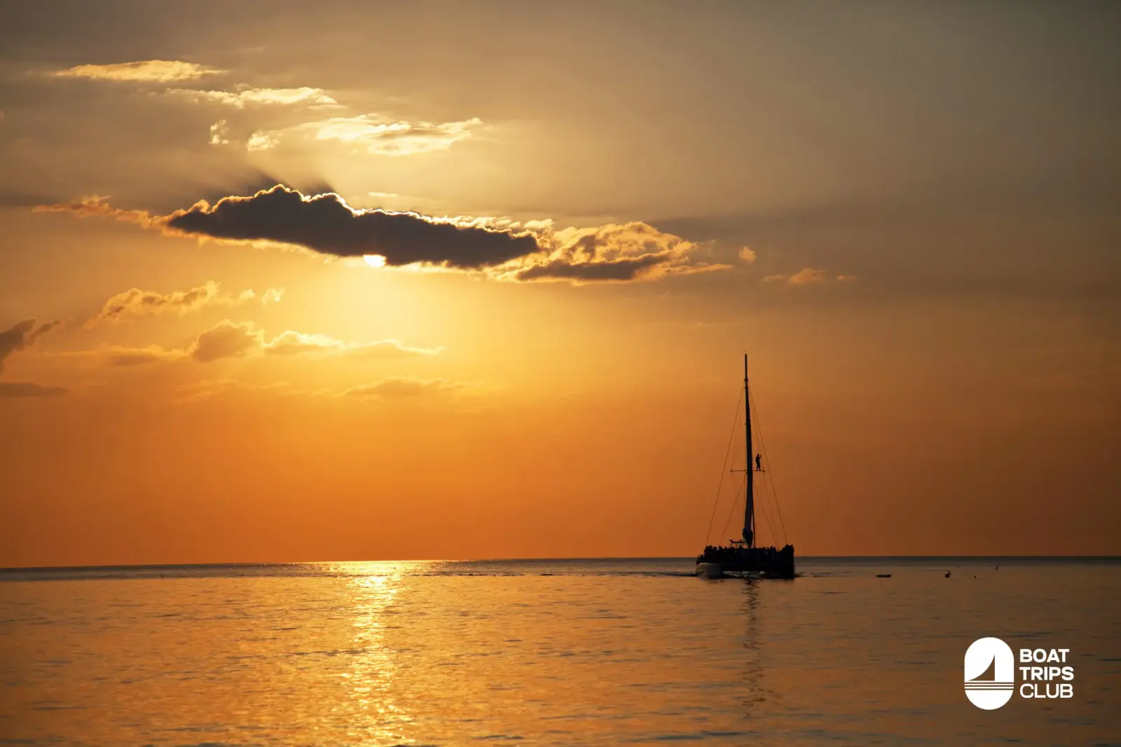 Silhouette of a sailing catamaran on golden water off Punta Cana as the sun sinks behind clouds