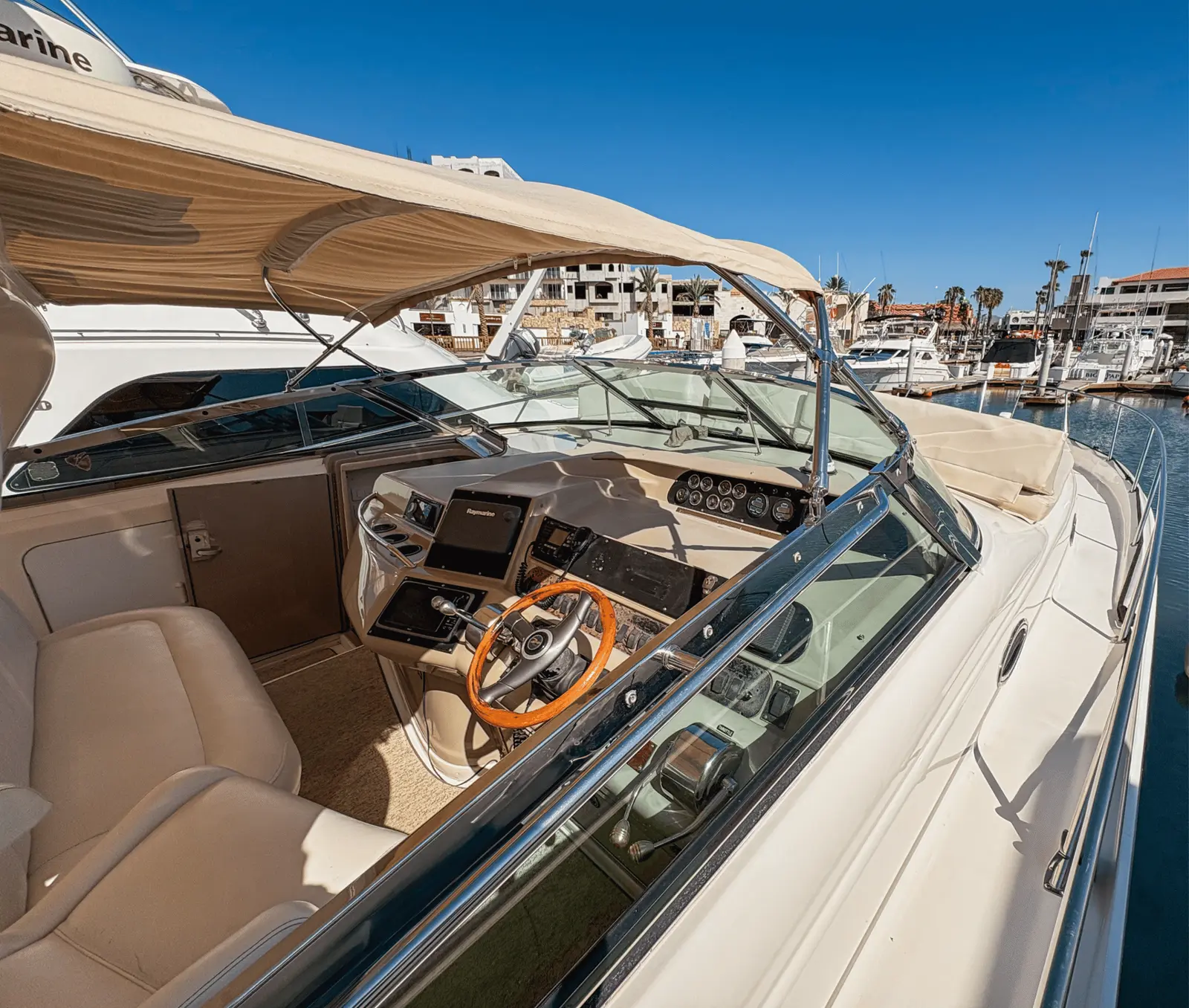 Helm of a motor yacht with a wooden steering wheel and cream seats, docked in a Cabo San Lucas marina