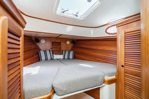 Picnic boat cabin with a V-berth in gray cushions, striped pillows, teak louvered doors and a hatch above