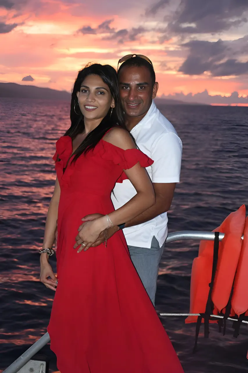 Couple in a red dress and white shirt posing on the catamaran deck under a pink sunset sky off Jamaica