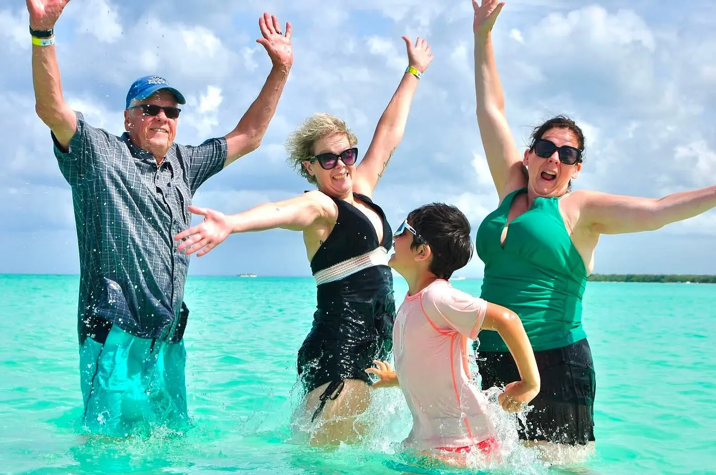 A family cheers with arms raised while standing waist-deep in turquoise water