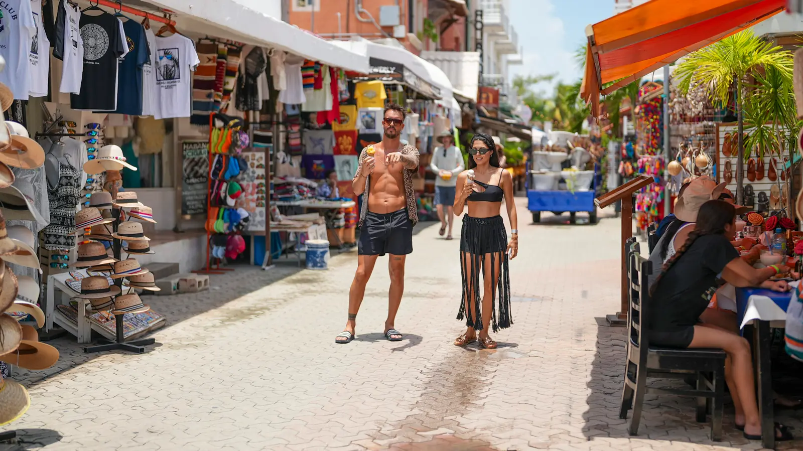 Couple strolling a pedestrian street of souvenir shops and straw hat stalls in Isla Mujeres town