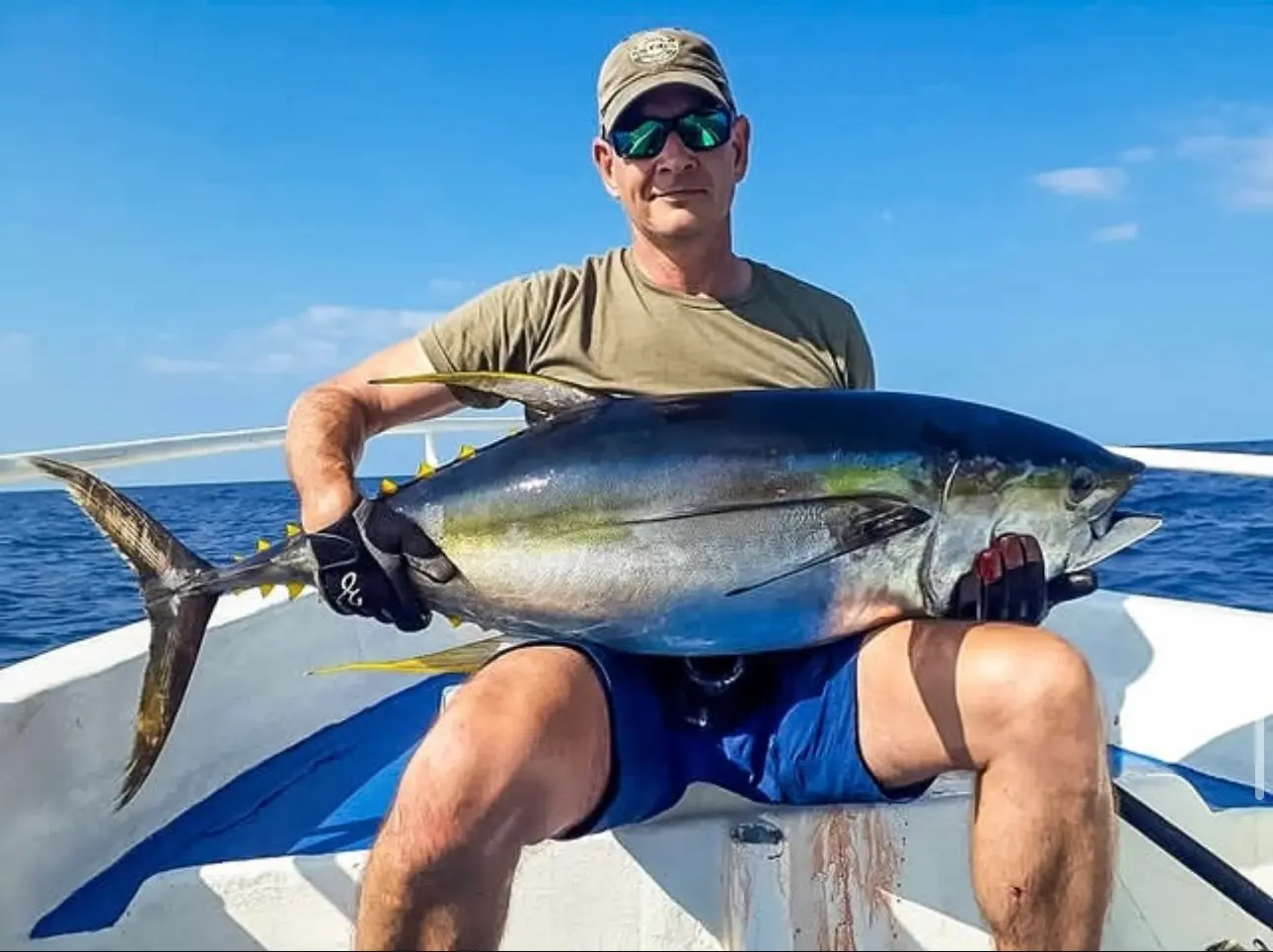 Angler in a cap and sunglasses holding up a large yellowfin tuna on the deck of a sportfishing boat