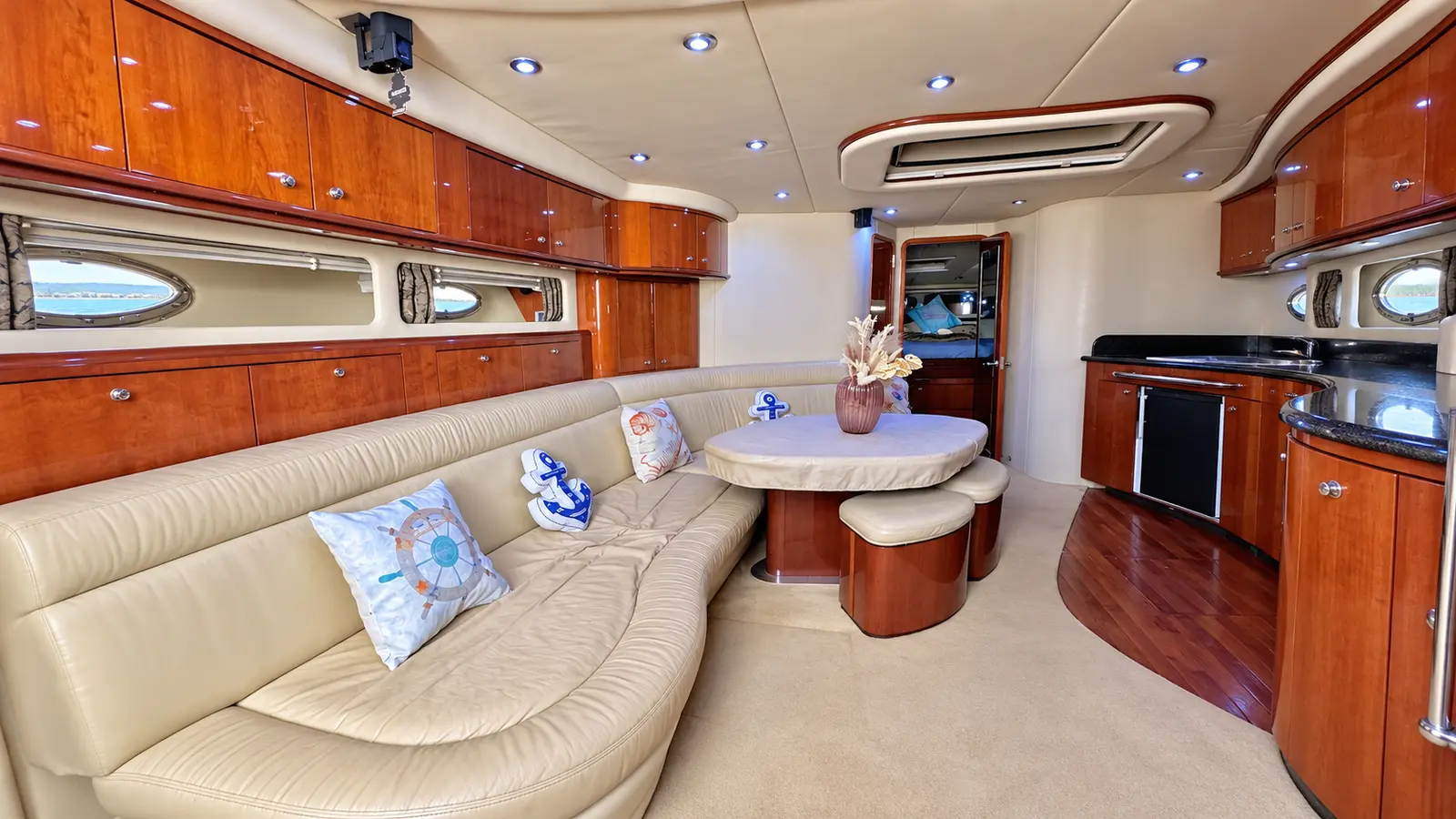 Saloon of a motor yacht with a long cream leather sofa, cherry wood cabinets and a round table