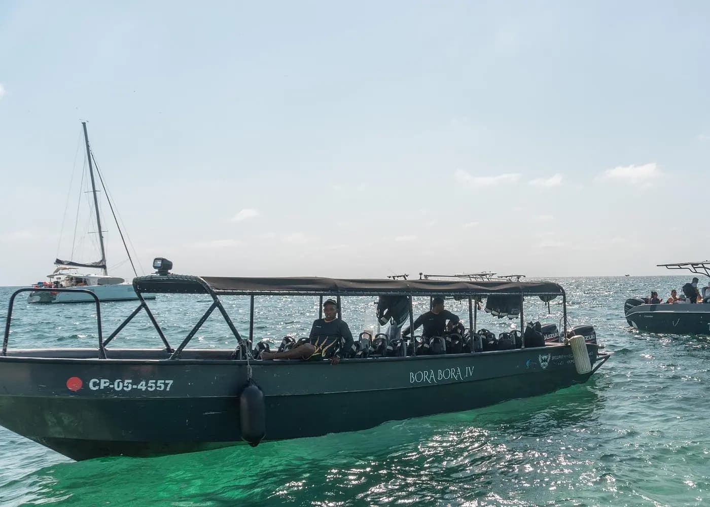 Gray covered speedboat with guests in life jackets on green water off Cartagena near a moored sailboat
