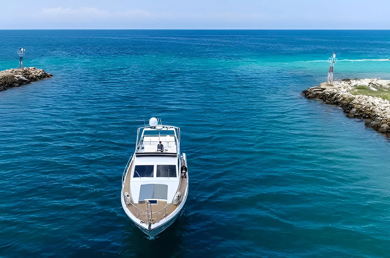 Aerial view of a white motor yacht passing between harbor breakwaters into the open sea off Mykonos