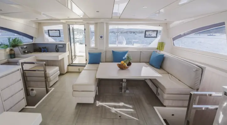 Wide view of the power catamaran salon with a U-shaped dinette, fruit bowl and galley counters