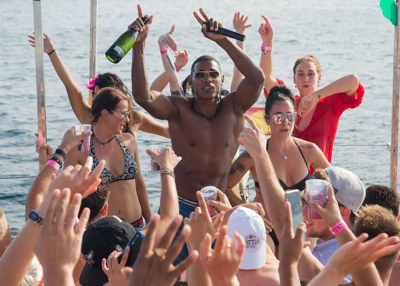 Shirtless man raising a bottle over a crowd of guests dancing with hands in the air