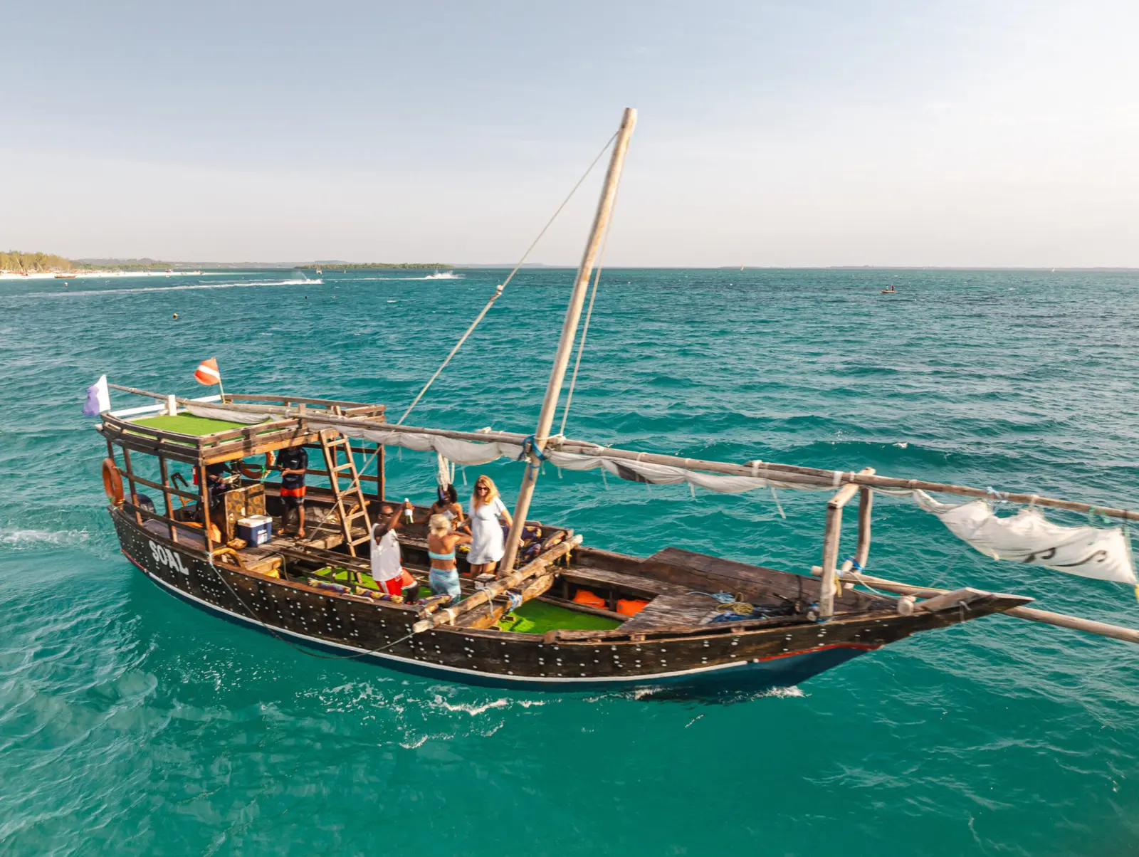 Guests on the open deck of a wooden dhow cruising through turquoise water off Zanzibar's north coast