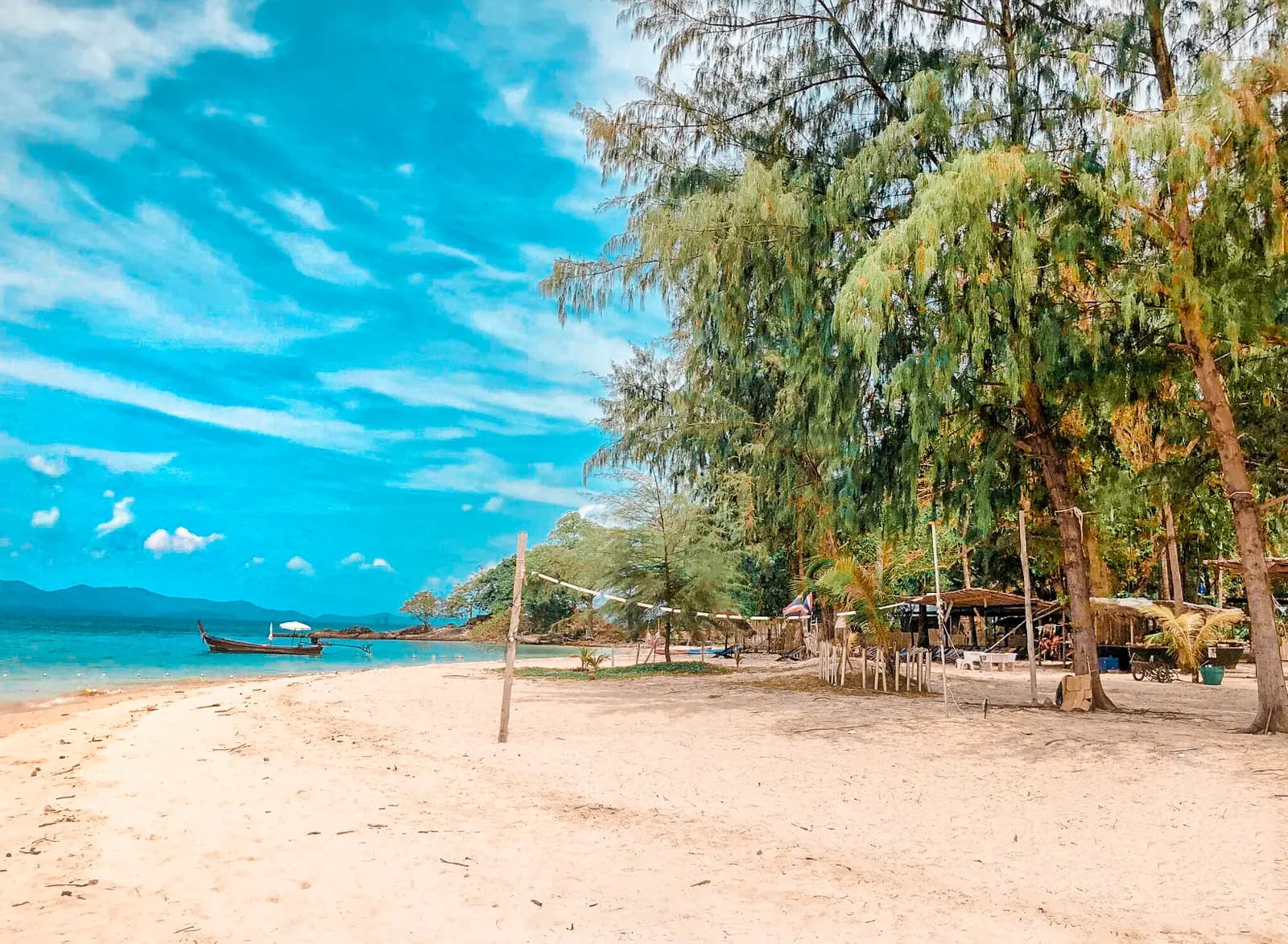 Quiet sandy beach shaded by leafy trees with boats moored offshore on a Khai island