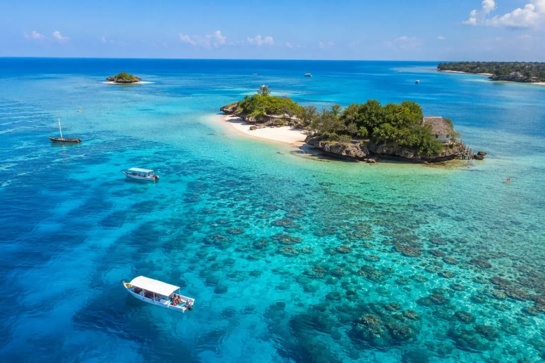 Best snorkeling in Zanzibar showcased through an aerial view of turquoise waters, coral reefs, small islands, and boats in the Indian Ocean.