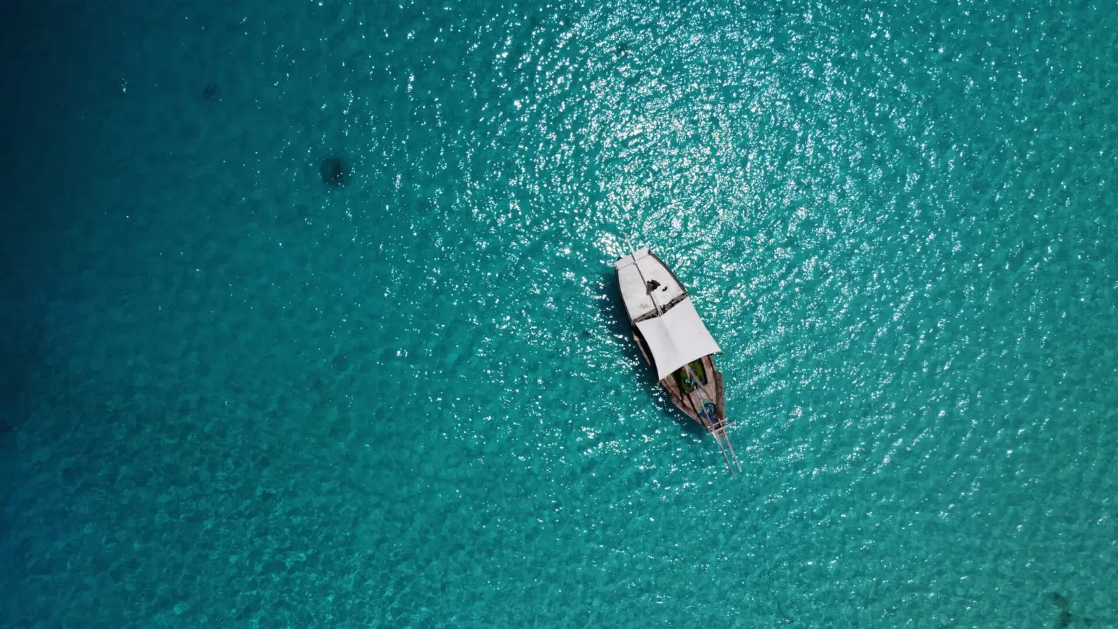 Top-down view of a lone dhow with a white canopy anchored on deep teal water off Zanzibar
