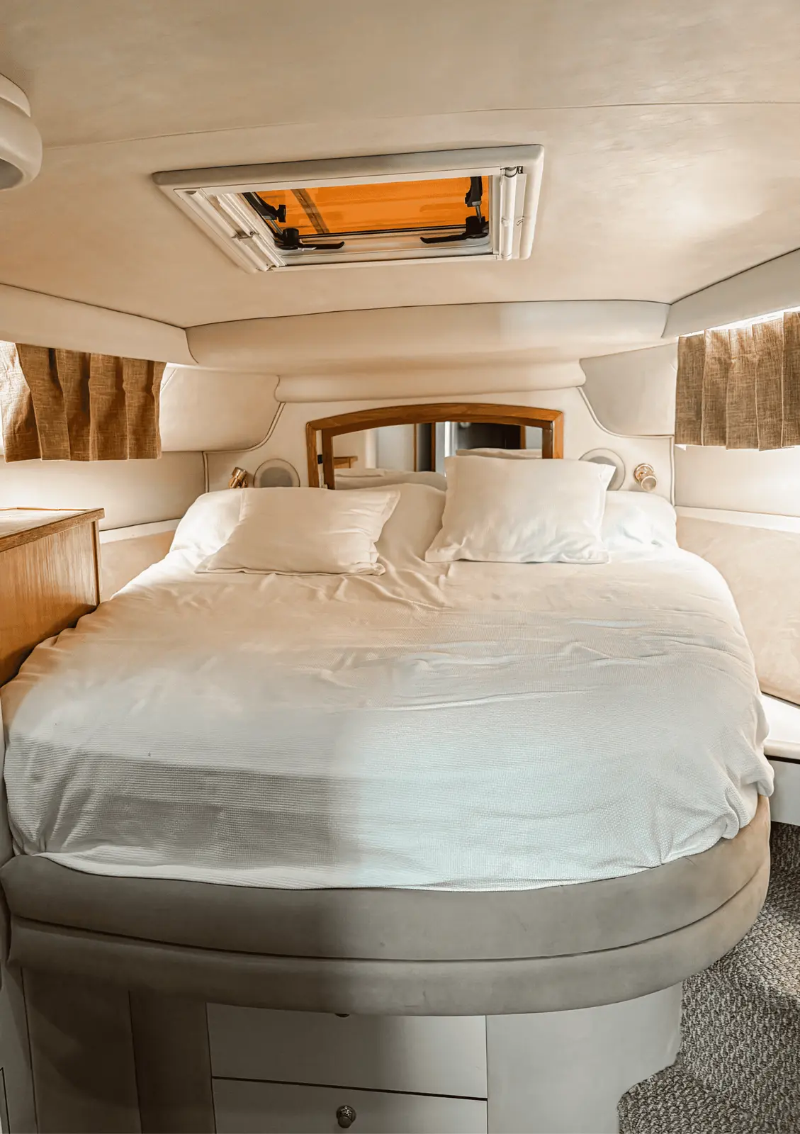 Yacht's forward cabin with a white-sheeted bed beneath an overhead hatch