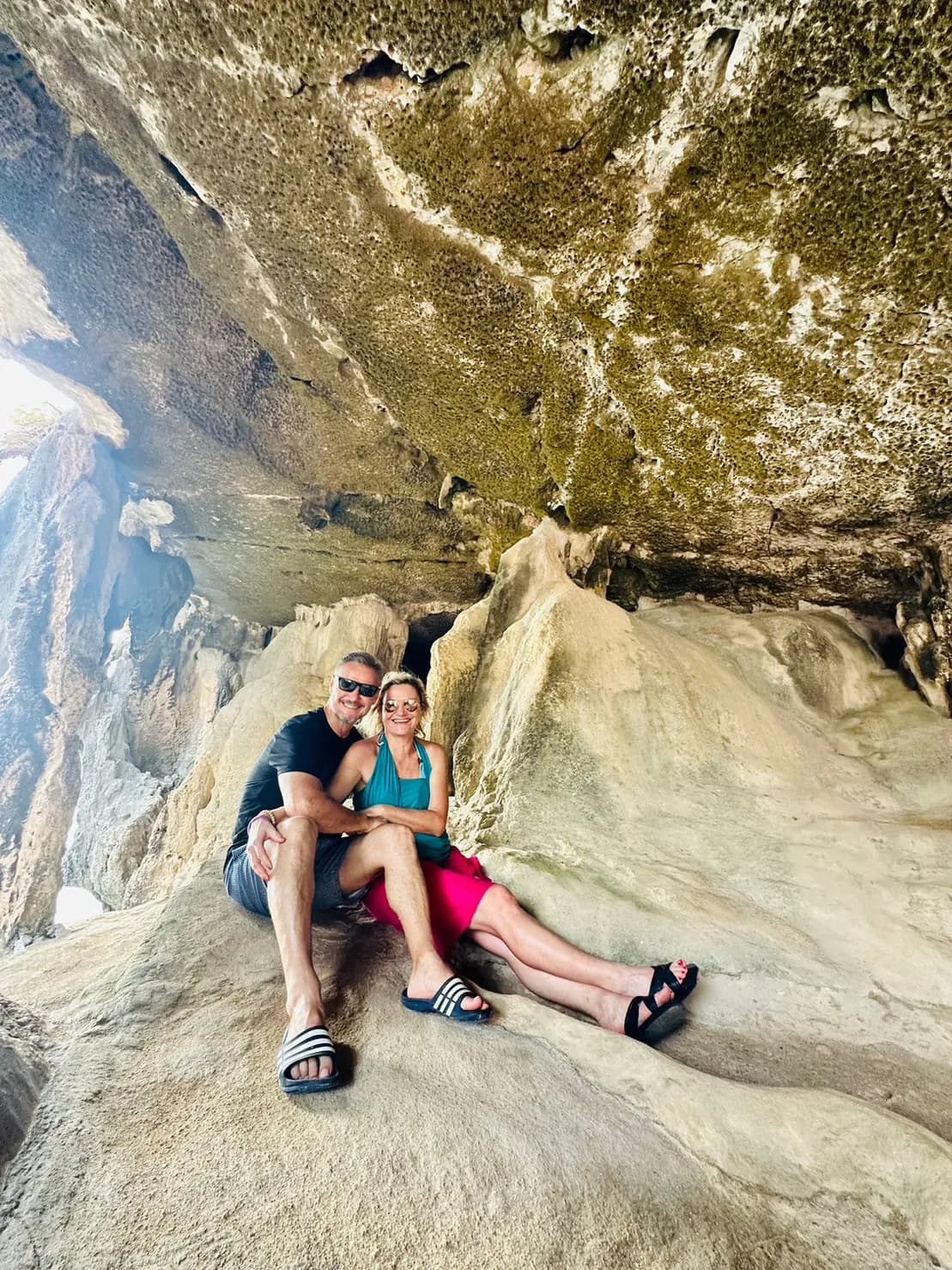 Couple sitting together on smooth rock beneath the ceiling of a limestone cave in Thailand