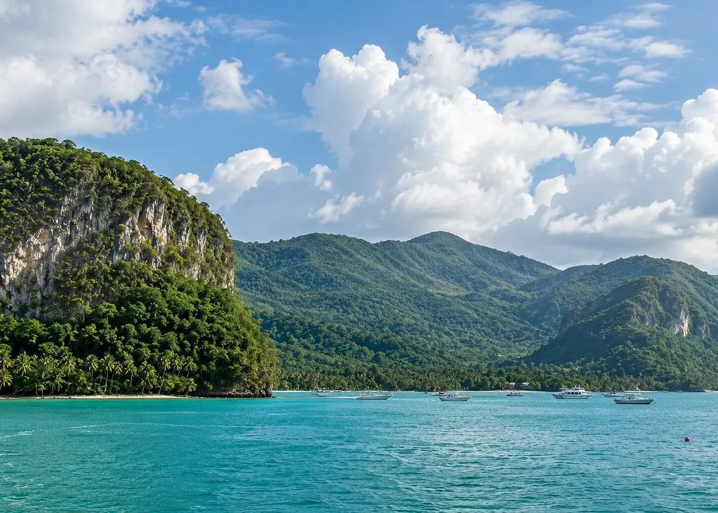 Jungle-covered cliffs and green mountains rising behind the turquoise water of Samaná Bay