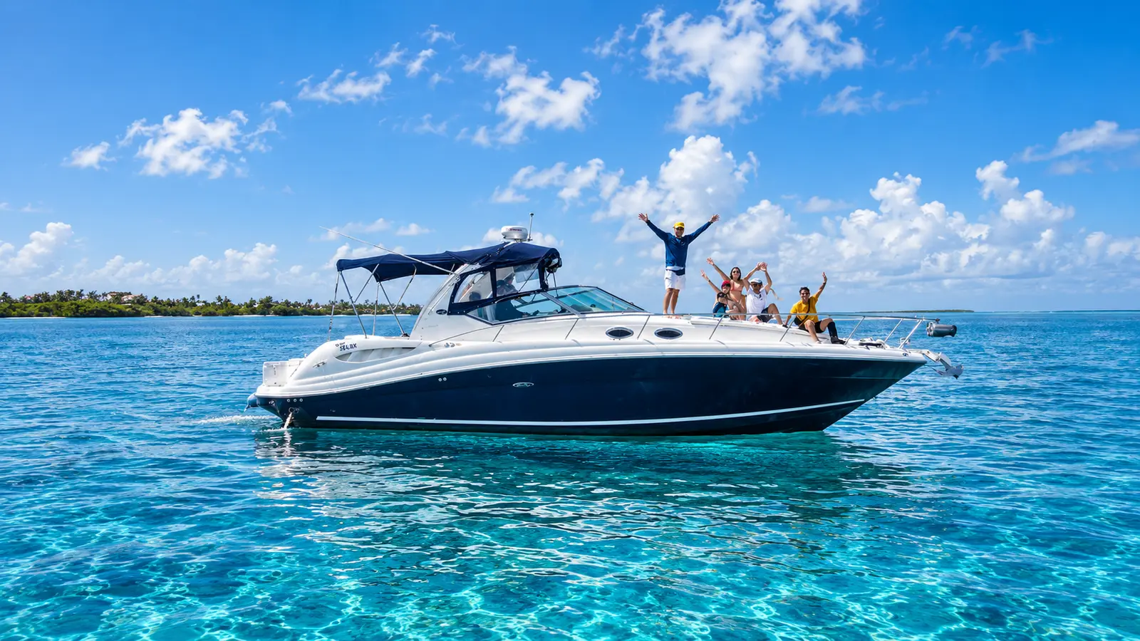 Motor yacht anchored in clear shallows near Cancún, guests cheering on the bow, palm-lined shore behind