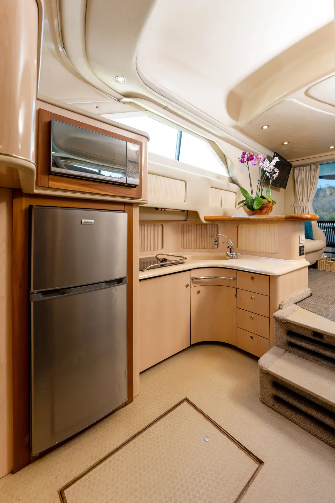 Yacht galley with a stainless steel fridge, microwave, wood cabinets and an orchid