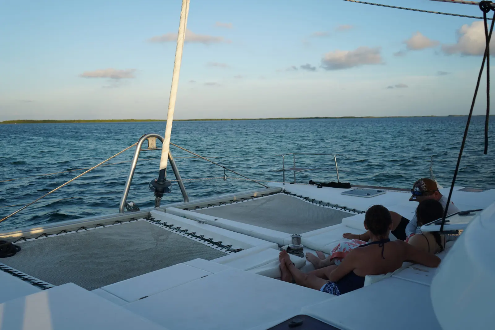 Twin trampoline nets on a catamaran bow with guests lounging nearby on the open sea