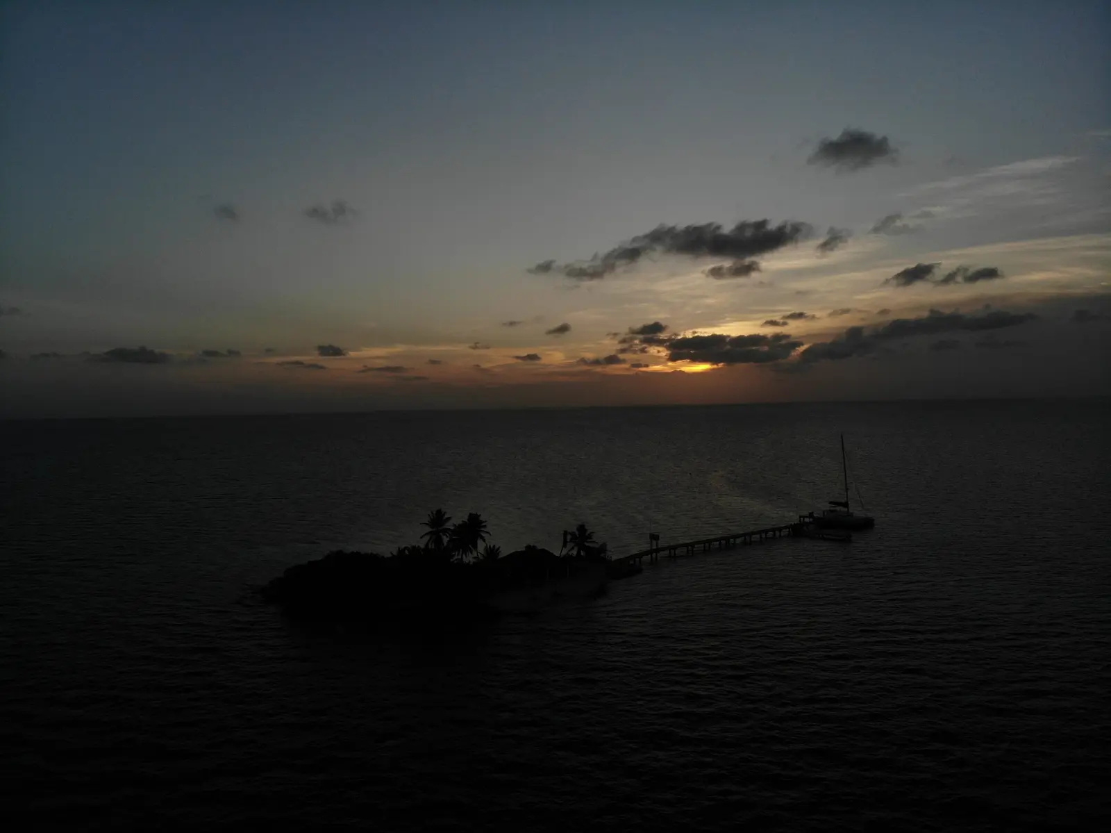 Small Belize caye, its pier and a moored sailboat silhouetted against the dusk sky