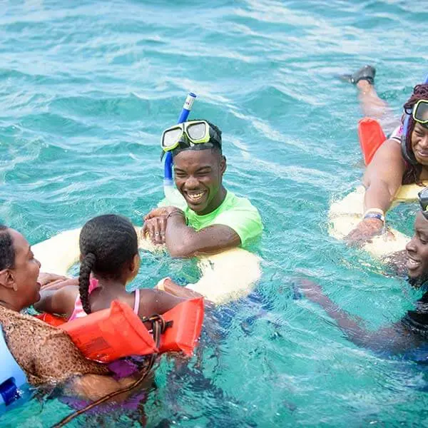 Snorkelers floating on foam noodles, a girl in an orange life vest beside a smiling man