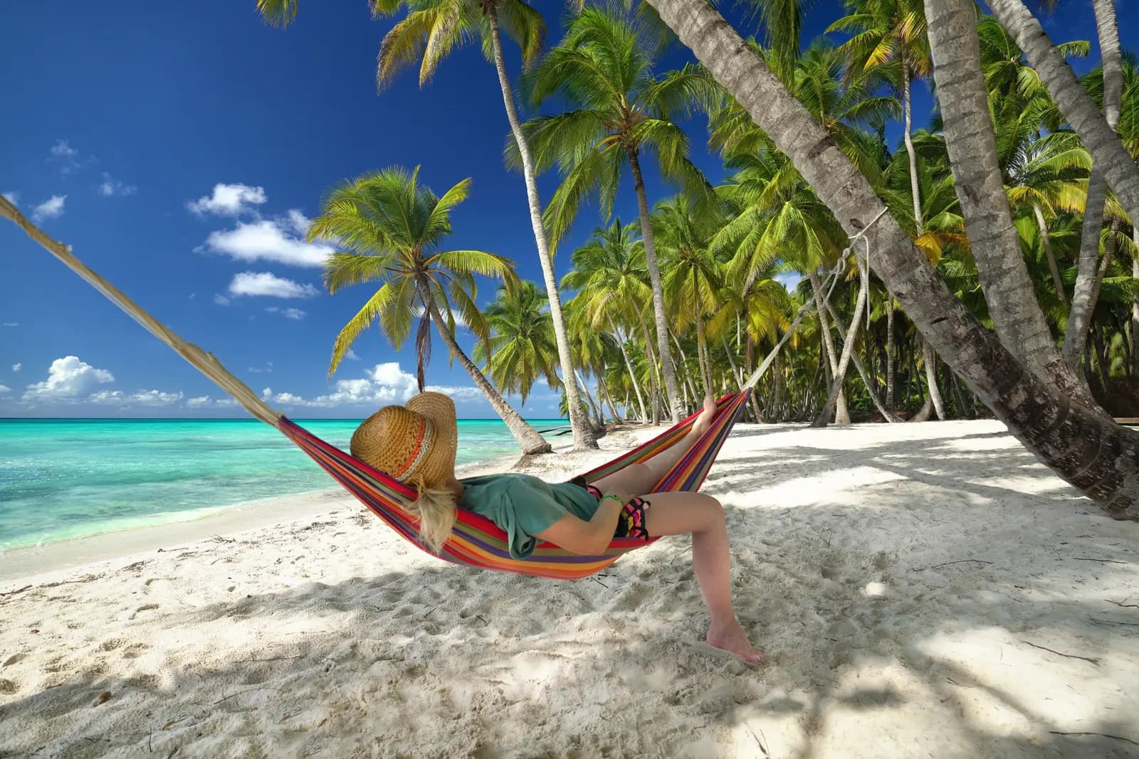 Woman in a straw hat lounging in a striped hammock under leaning palms on a Saona Island beach
