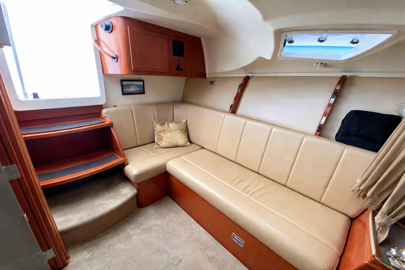 Cabin of a sportfishing boat with a cream wraparound sofa and wooden steps up to the deck