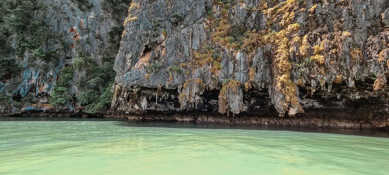 Overhanging limestone cliff with dripstone formations above calm green water in Thailand