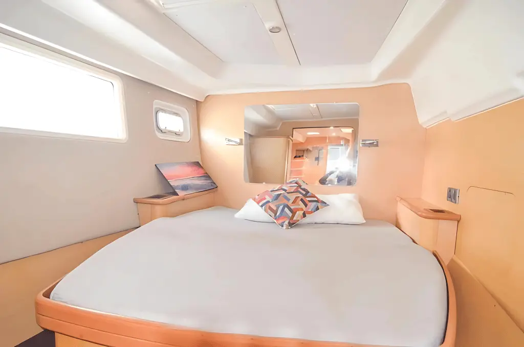 Guest cabin with a double bed, light wood paneling and small hull windows inside a power catamaran