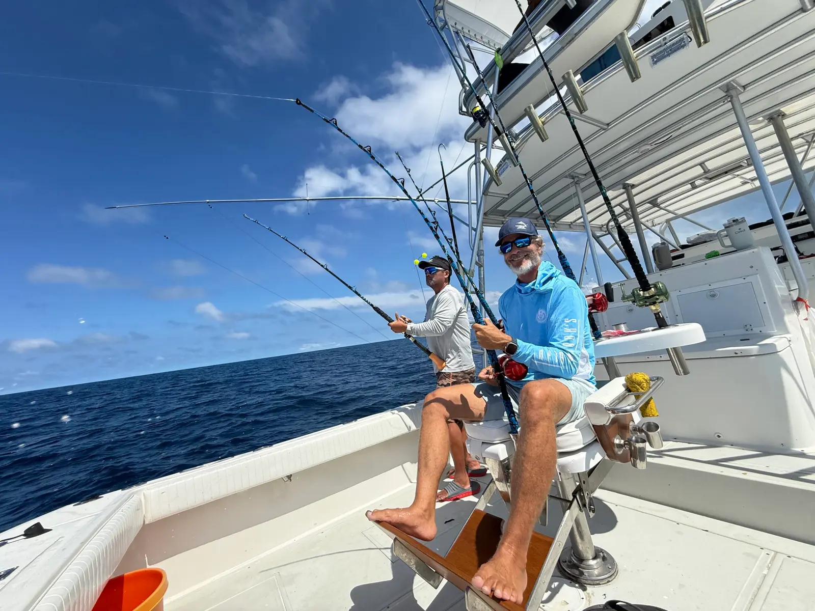Two anglers with rods on the deck of a sportfishing boat, one seated in the fighting chair