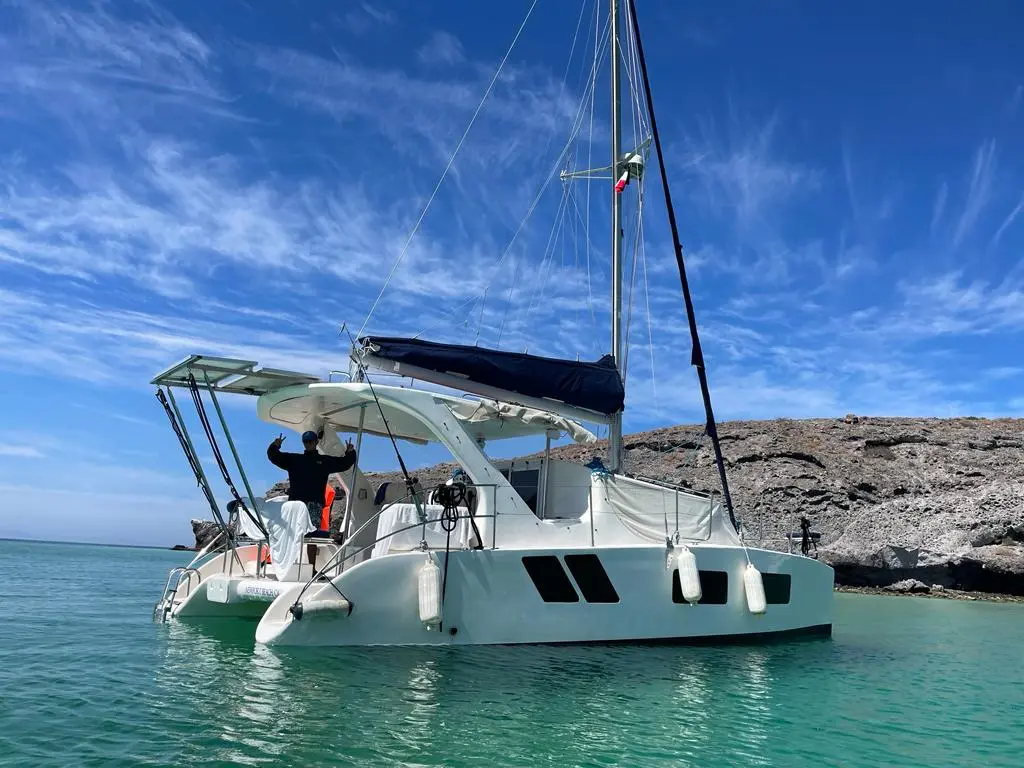 Sailing catamaran anchored in calm clear water beside a rocky shoreline near La Paz
