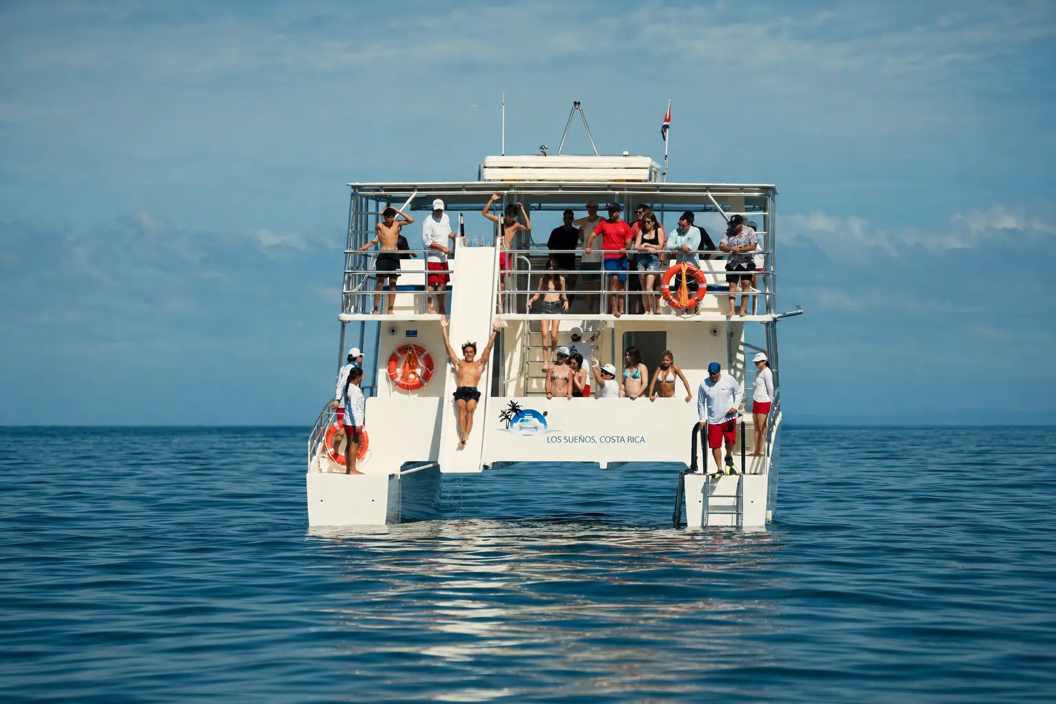 Stern view of a two-deck catamaran on calm water off Costa Rica as a guest raises both arms on the water slide