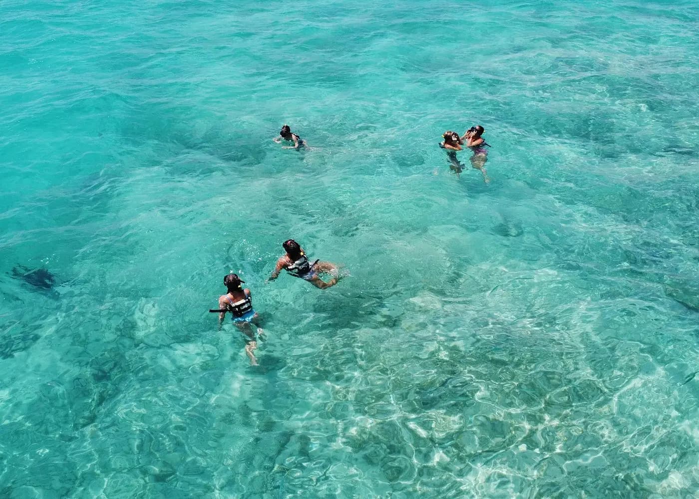 Snorkelers in life vests swimming in clear turquoise water over a sandy reef