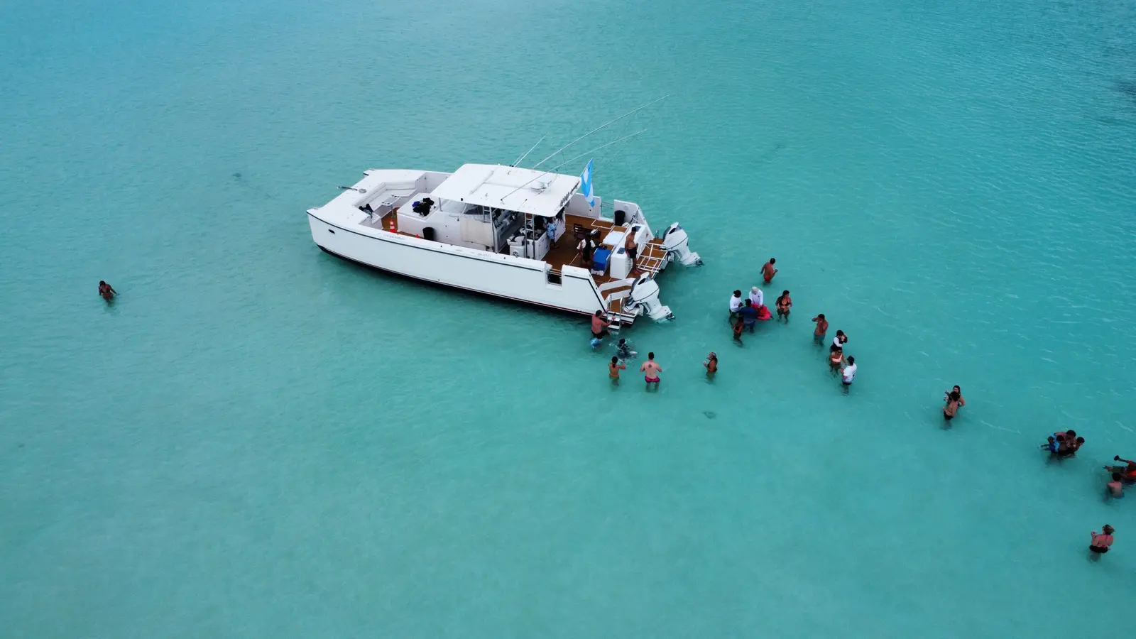 Guests wading in waist-deep turquoise water beside an anchored power catamaran at the Saona Island sandbank