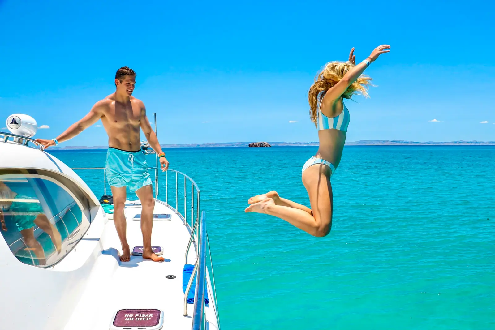 A woman jumps off the side deck of the power catamaran into turquoise water as a man watches