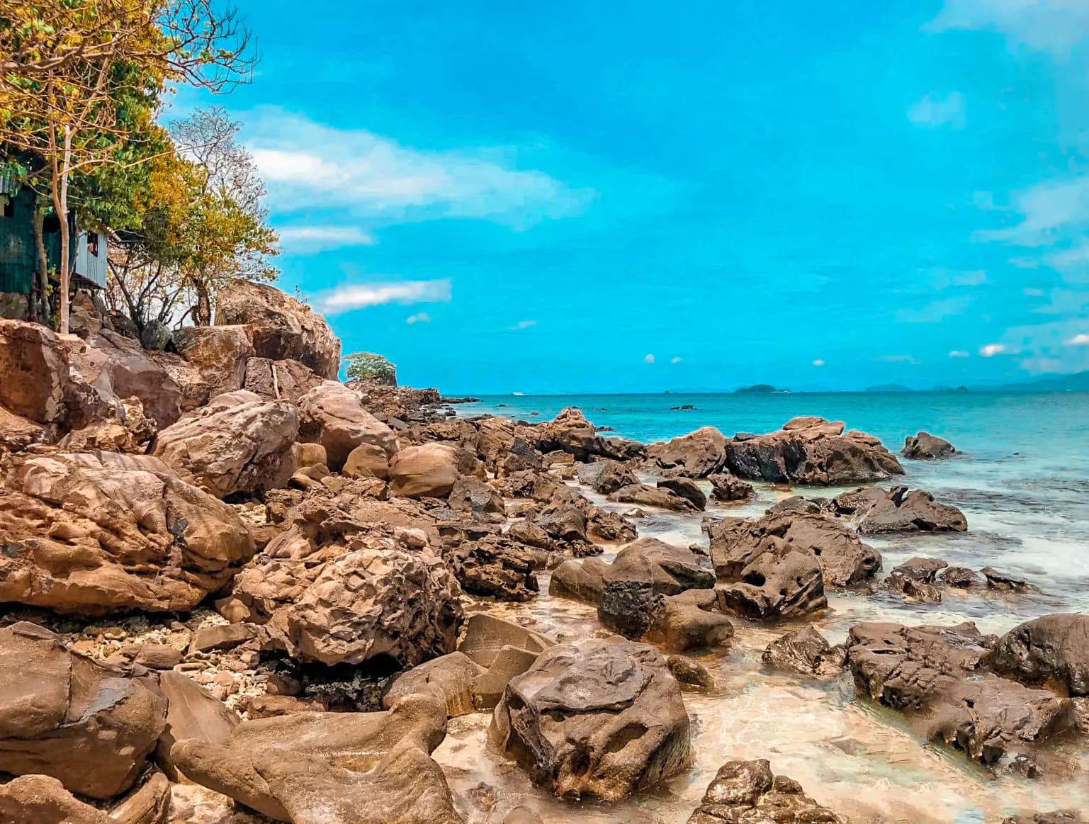 Sun-baked brown boulders piled along a Khai island shore beside a turquoise sea and blue sky