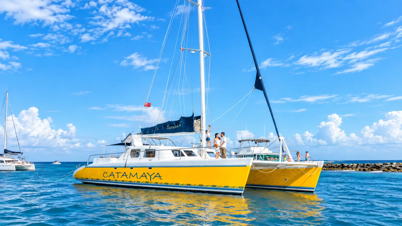 Two yellow sailing catamarans moored side by side in calm blue water near a Riviera Maya breakwater
