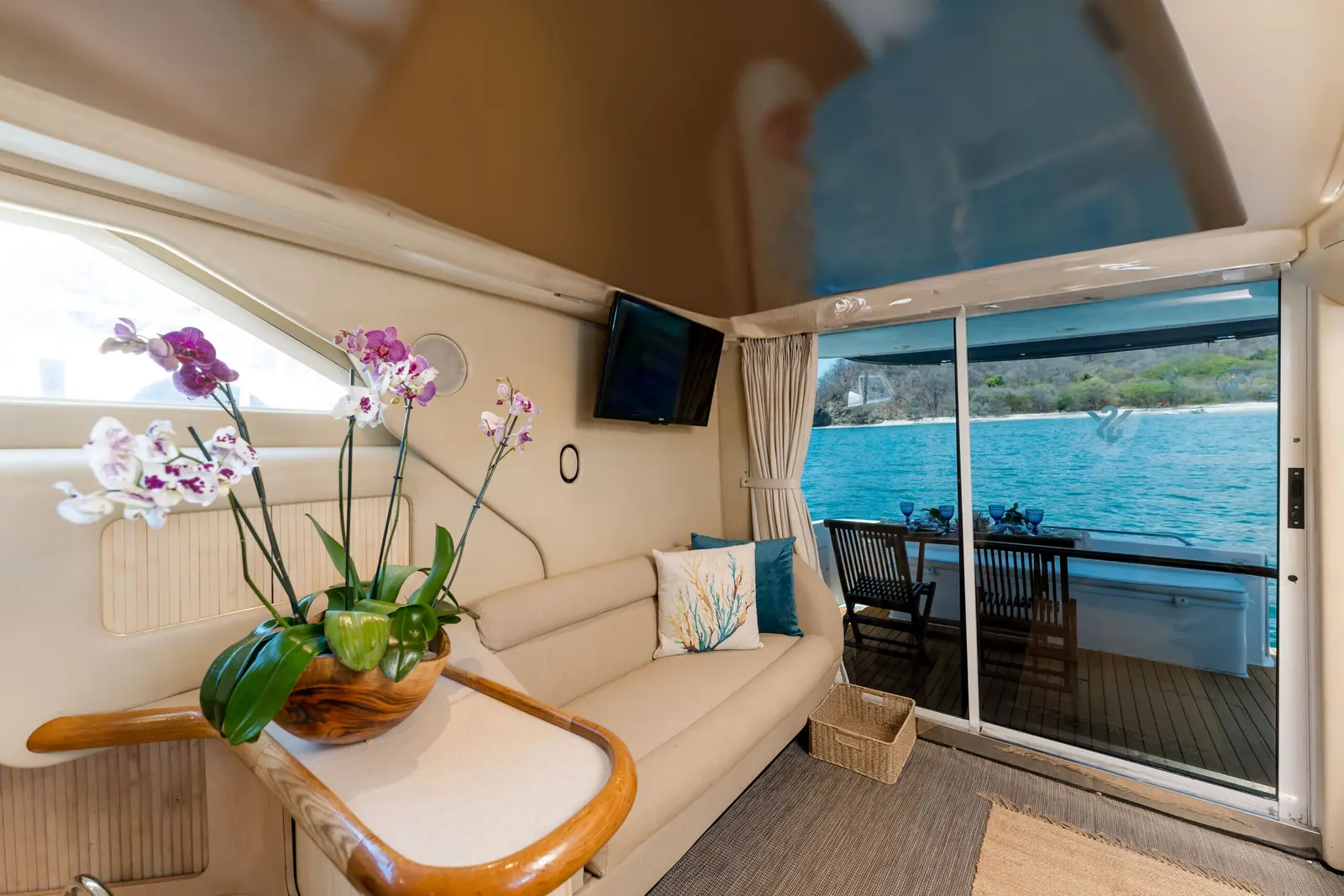 Yacht salon with orchids, a cream sofa and sliding glass doors open to the aft deck and sea