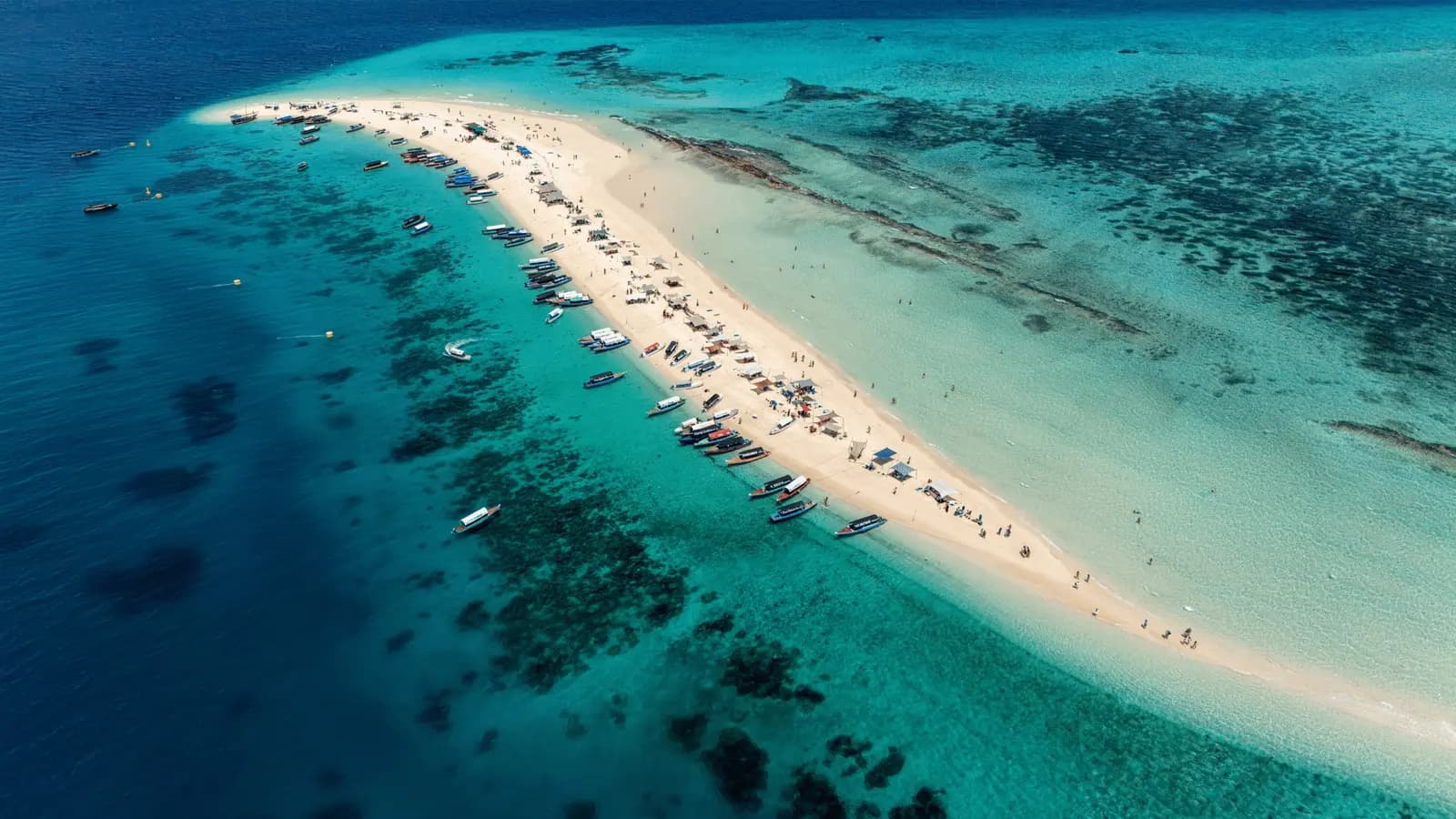 Long, narrow white sandbank lined with anchored boats and visitors, seen from above off Zanzibar