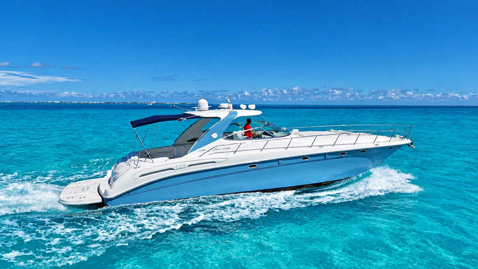 White motor yacht with a dark bimini top speeding over deep blue water, Cancún skyline on the horizon