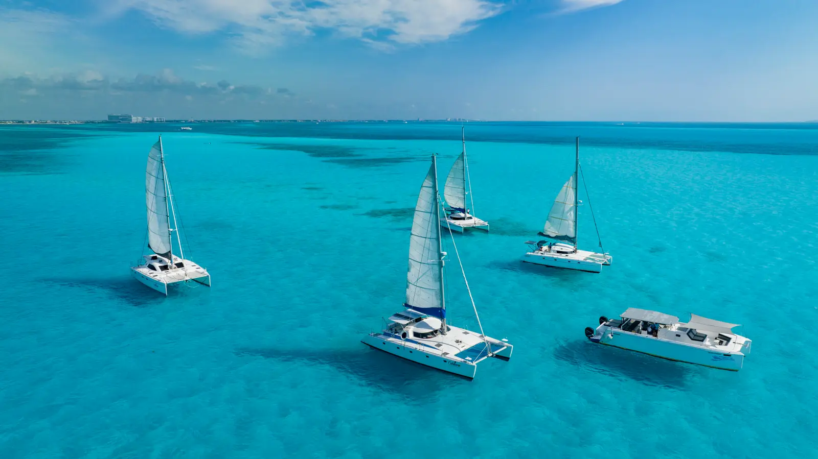 Sailing catamarans and a yacht on turquoise water off Cancún