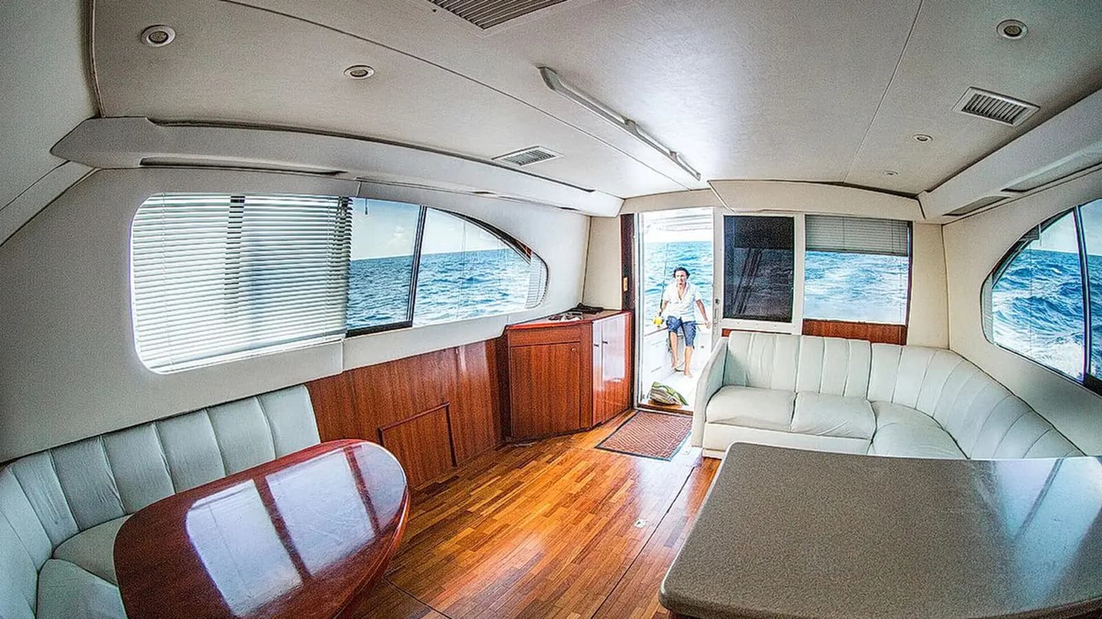 Salon of a sportfishing boat with cream leather sofas, teak floors and windows onto the sea