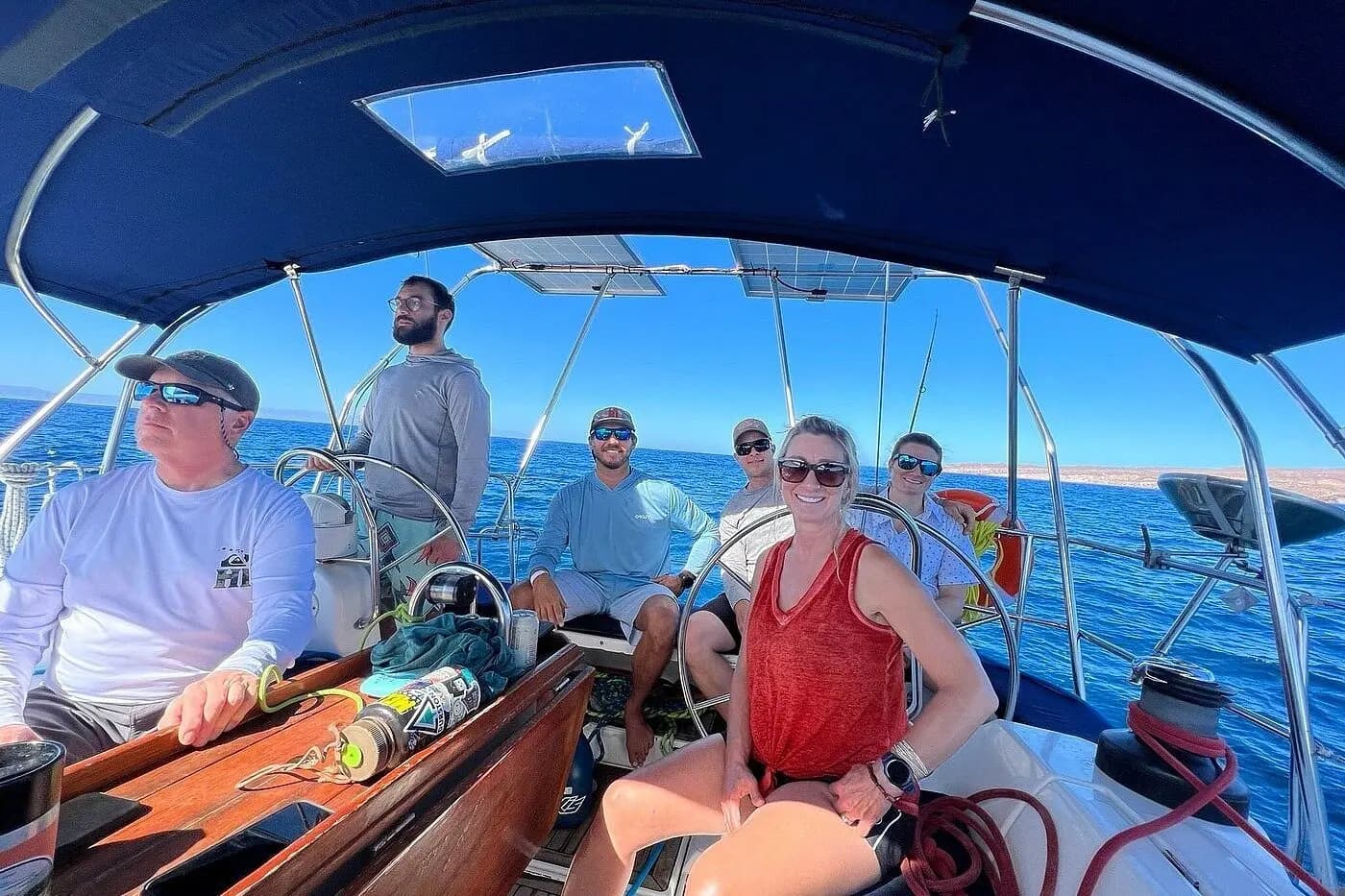 Guests seated in the cockpit of a sailboat under a blue bimini on the Sea of Cortez