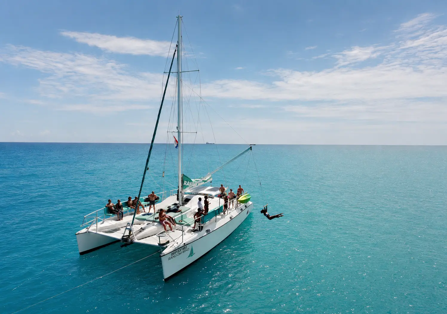 Guest dropping off the rope swing beside a sailing catamaran anchored in calm turquoise water off St. Maarten